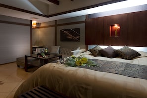 A modern hotel room with a large bed, a sitting area with a table and chairs, and a wall-mounted TV.