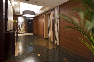 Un moderno vestíbulo de hotel con piso de piedra pulida, paneles de madera y una gran lámpara de candelabro.
