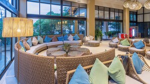 Un espacio interior amplio con mobiliario de mimbre, ventanas grandes y una lámpara colgante.