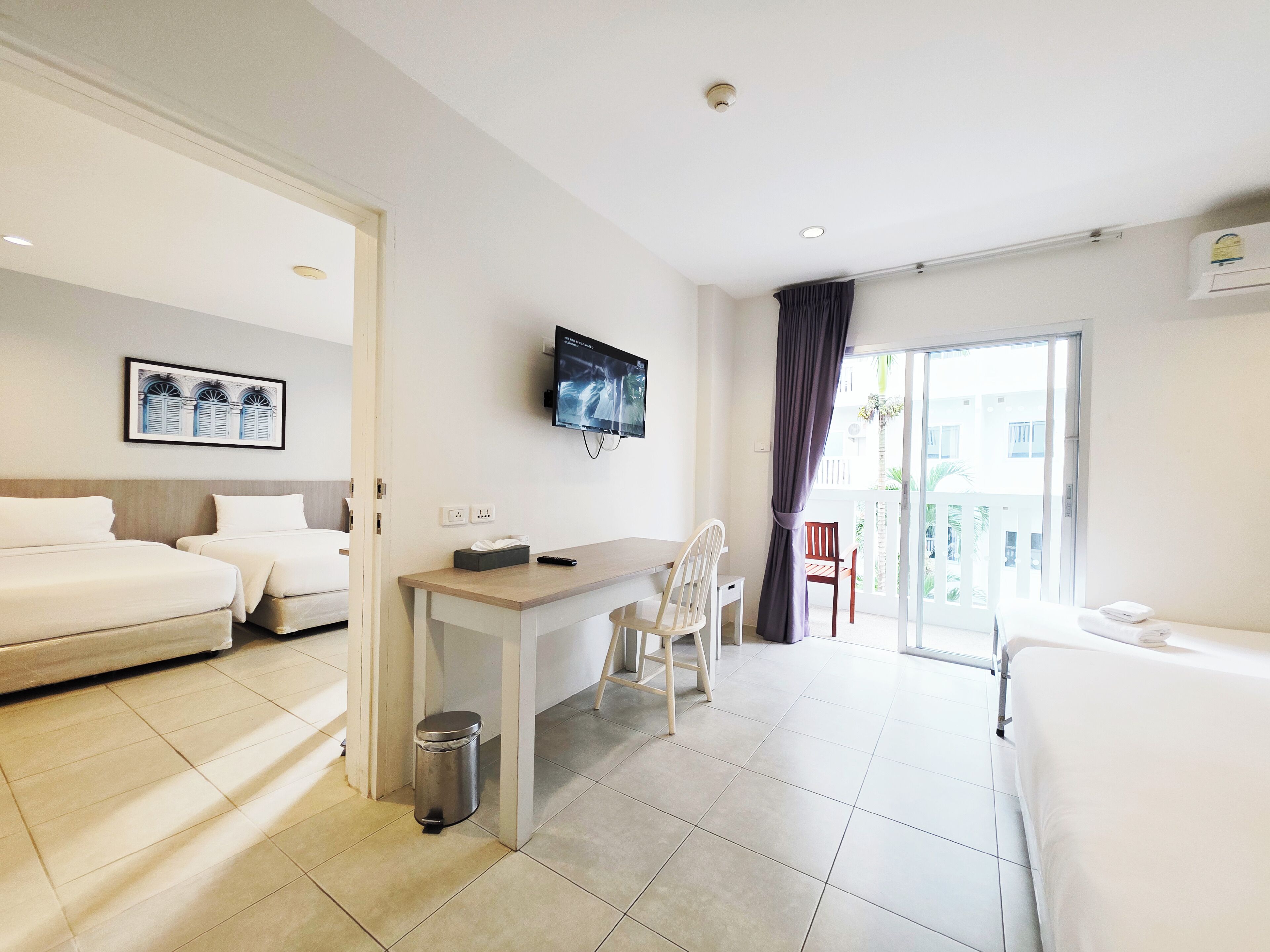 A hotel room with two beds, a desk, a chair, a TV, and a balcony with a view.