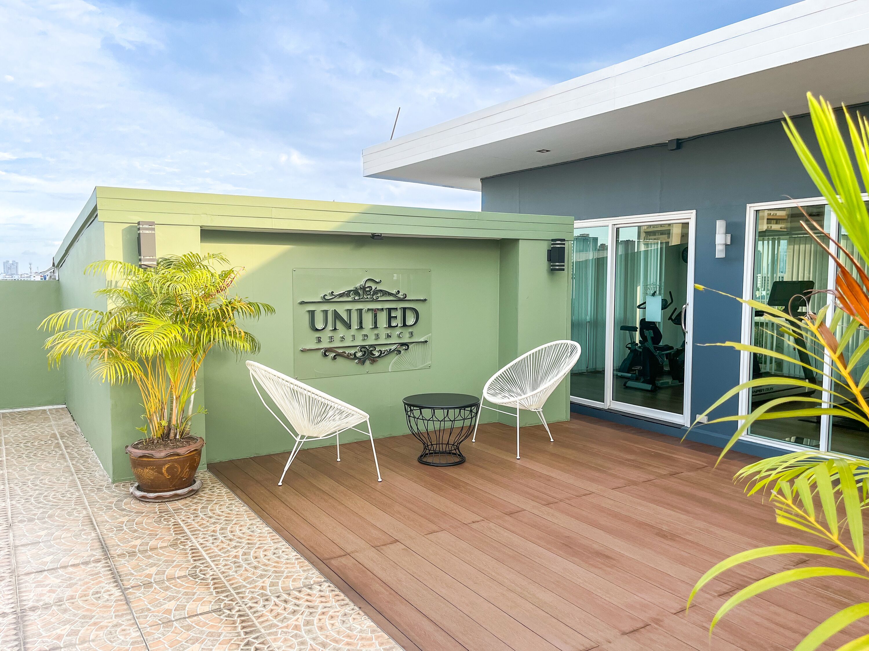 Ett modernt utomhusområde med sittplatser, en grön vägg, en krukväxt och en skylt med texten ”UNITED RESIDENCE”.
