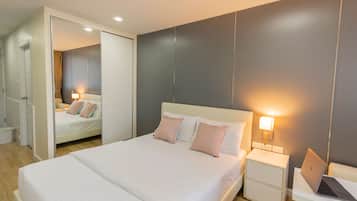 A modern hotel room with a large bed, bedside tables, a laptop, and a mirror.