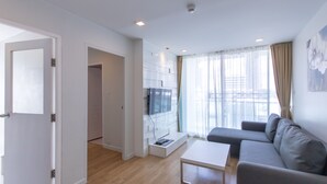 Uma sala de estar moderna com um sofá cinza, uma mesa de centro branca e uma TV montada em uma parede de vidro.