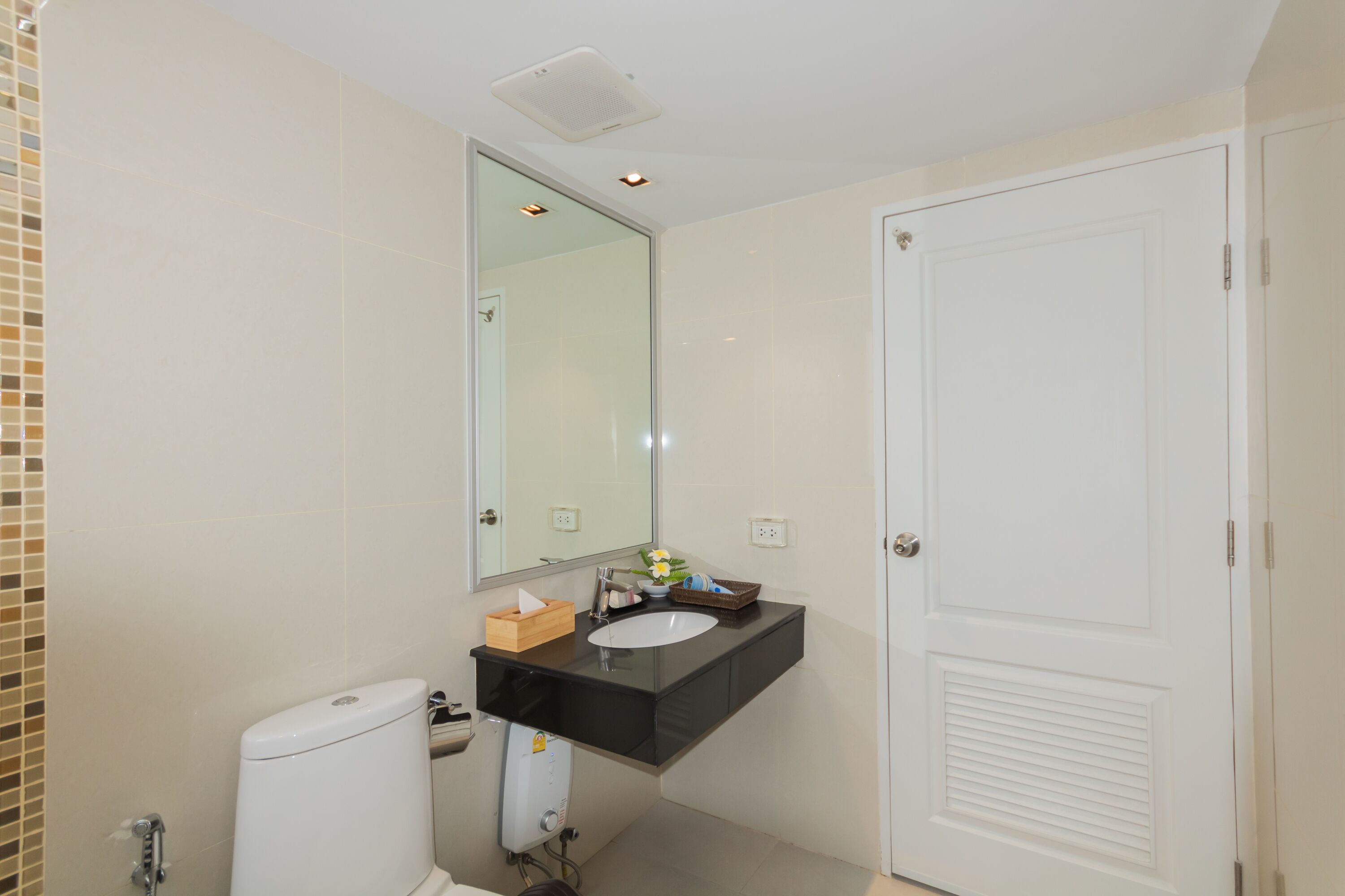 A bathroom with a white toilet, a black sink, a mirror, and a white door.
