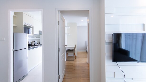 Cozinha moderna com geladeira, fogão e micro-ondas. Possui área de jantar com mesa e cadeiras. Uma TV de tela plana está fixada na parede.