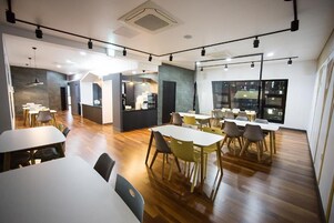 Un comedor moderno con varias mesas y sillas, una cocina al fondo y ventanas amplias.