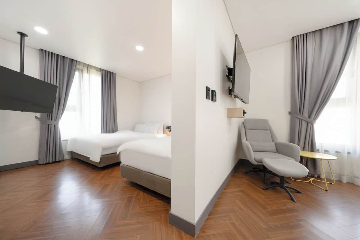 Ein modernes Hotelzimmer mit Bett, Schreibtisch, Stuhl, Fernseher und einem Fenster mit Vorhängen.