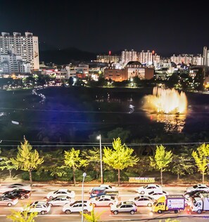 Un paisaje urbano nocturno con un río, edificios iluminados y un estacionamiento con automóviles.