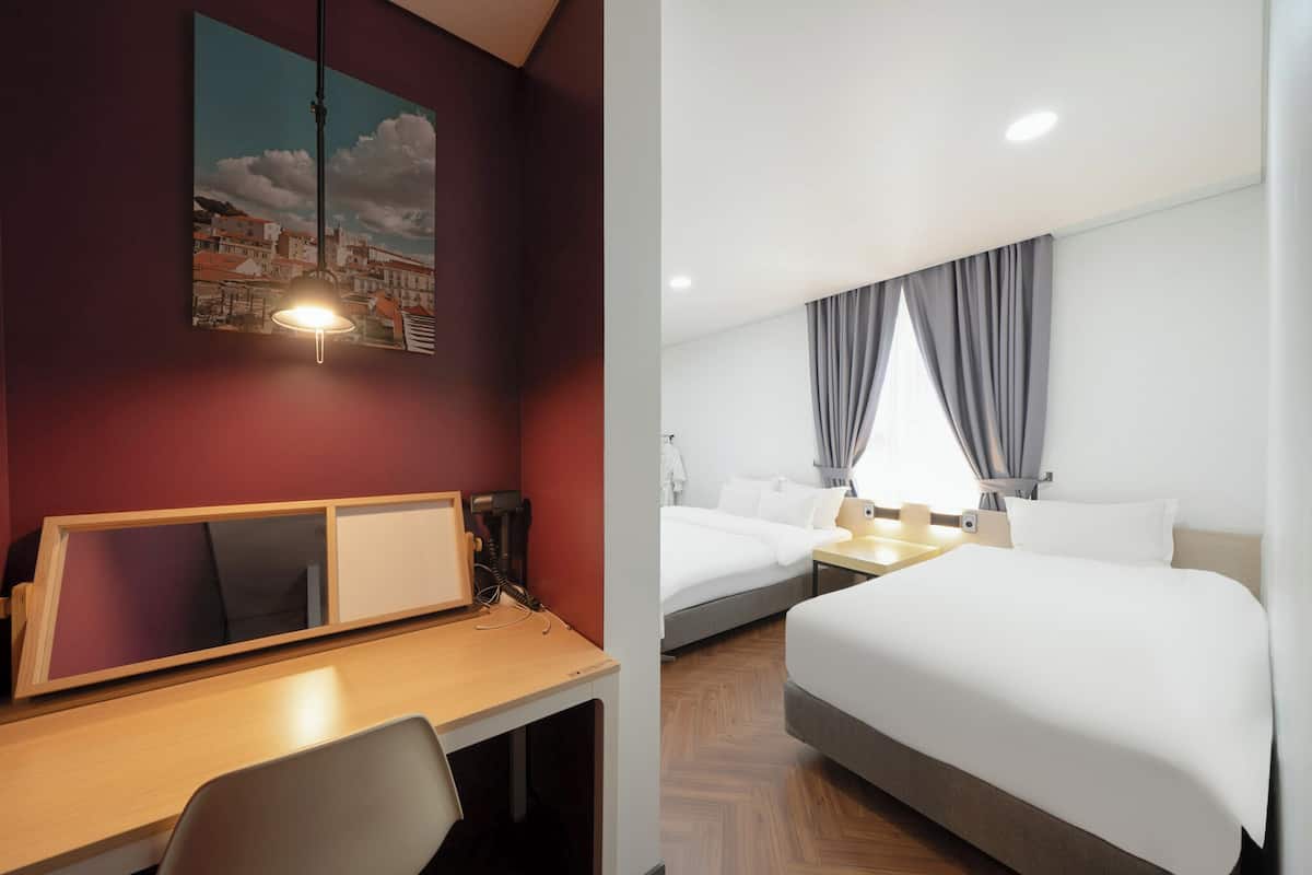 Ein Hotelzimmer mit Bett, Nachttisch, Lampe und Schreibtisch mit Stuhl.