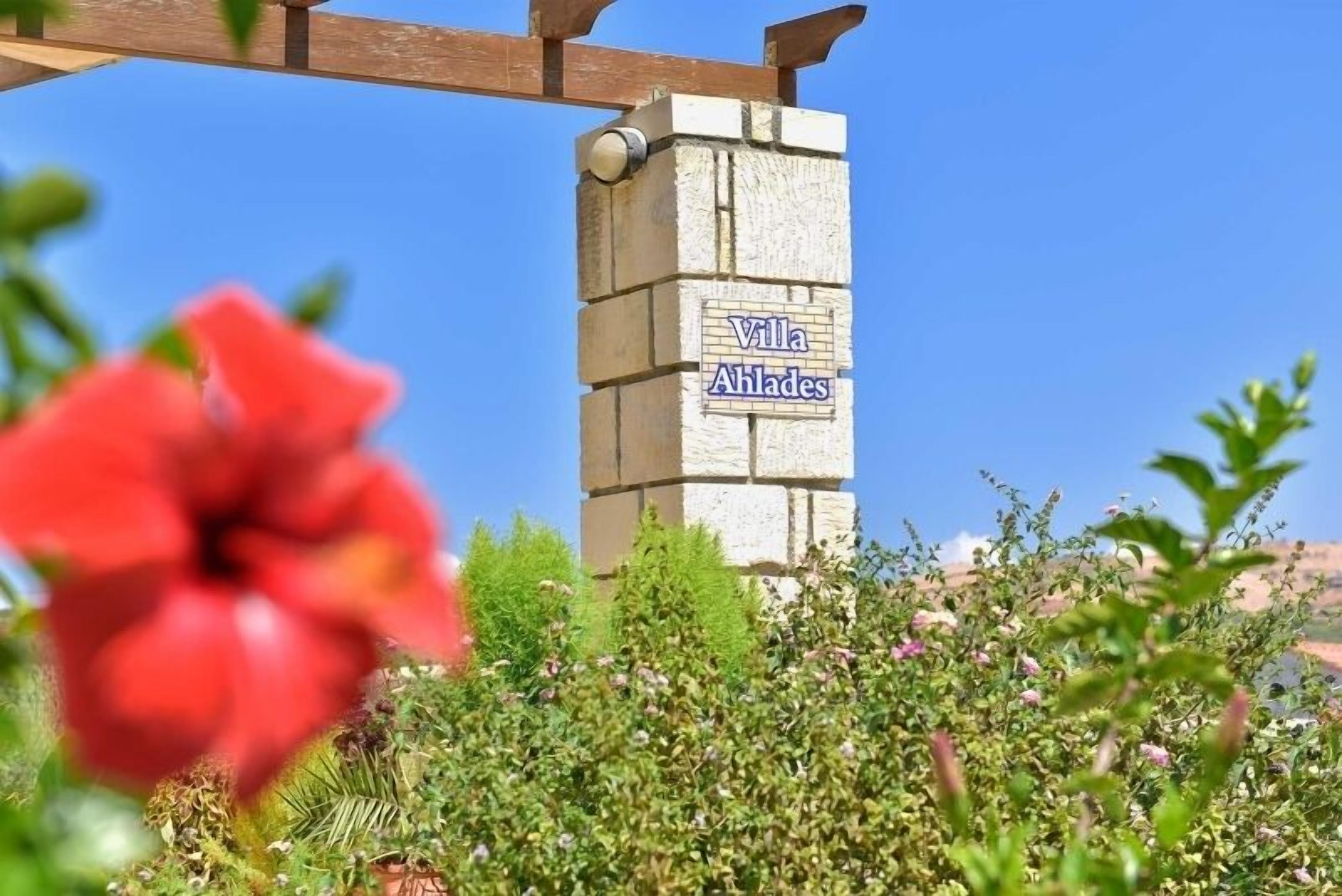 Un letrero de piedra con la inscripción 'Villa Ahlades', sobre un cielo azul despejado.