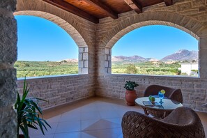 A terrace with stone arches, a table with chairs, a potted plant, and a view of a mountainous landscape.