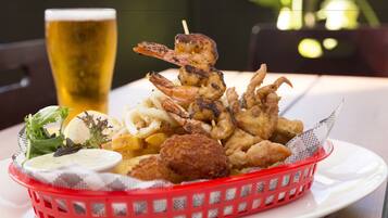 Una cesta de mariscos fritos, como camarones y calamares, una cerveza en un vaso, y una ensalada como guarnición sobre un plato blanco.