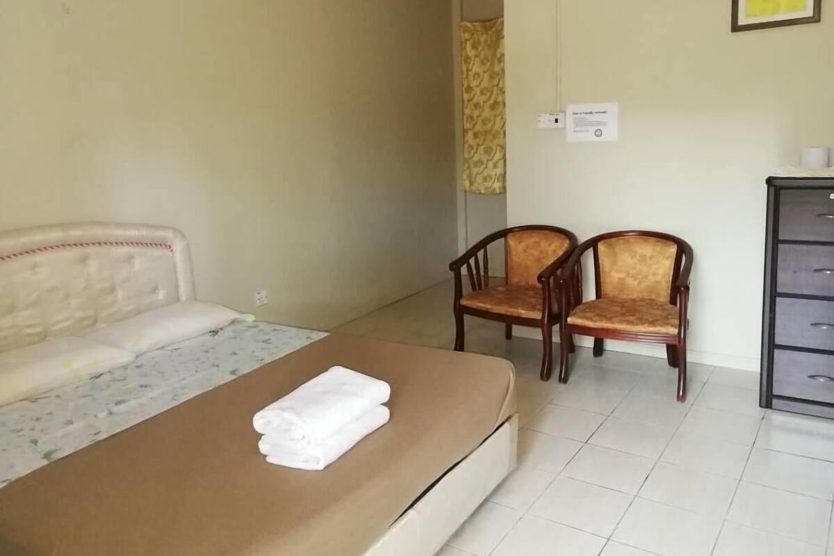 A hotel room with a bed, two wooden chairs, a dresser, and a wall-mounted light switch.
