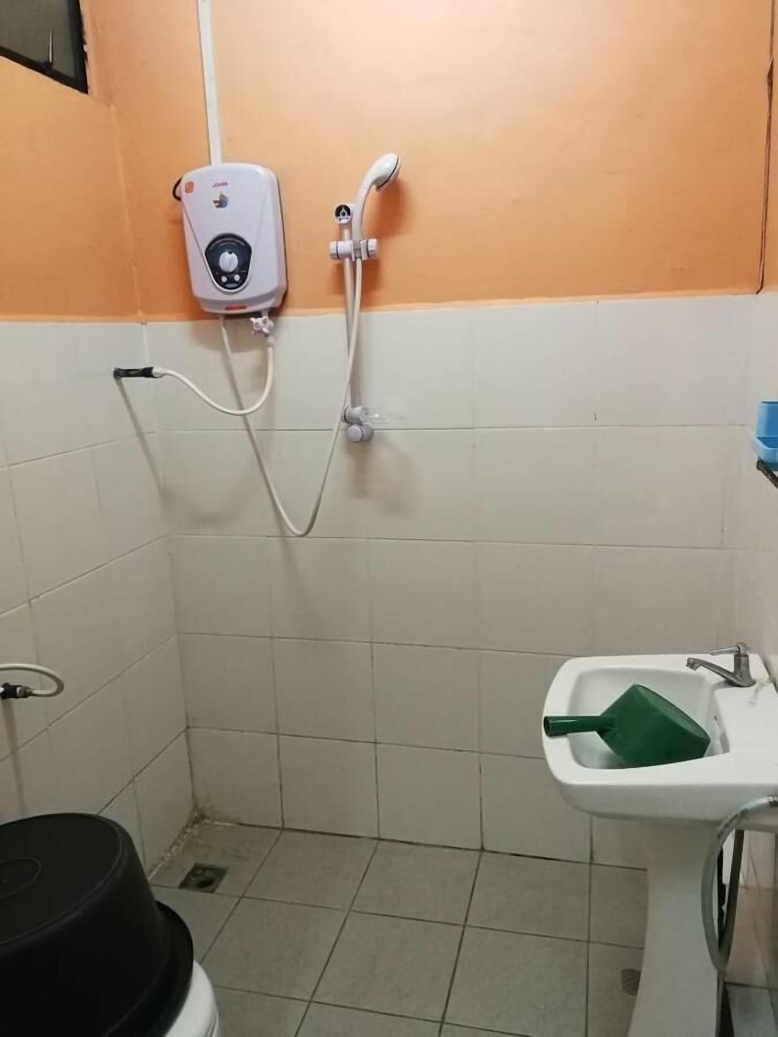 A small bathroom with a white sink, a green soap dispenser, and a handheld showerhead mounted on the wall.