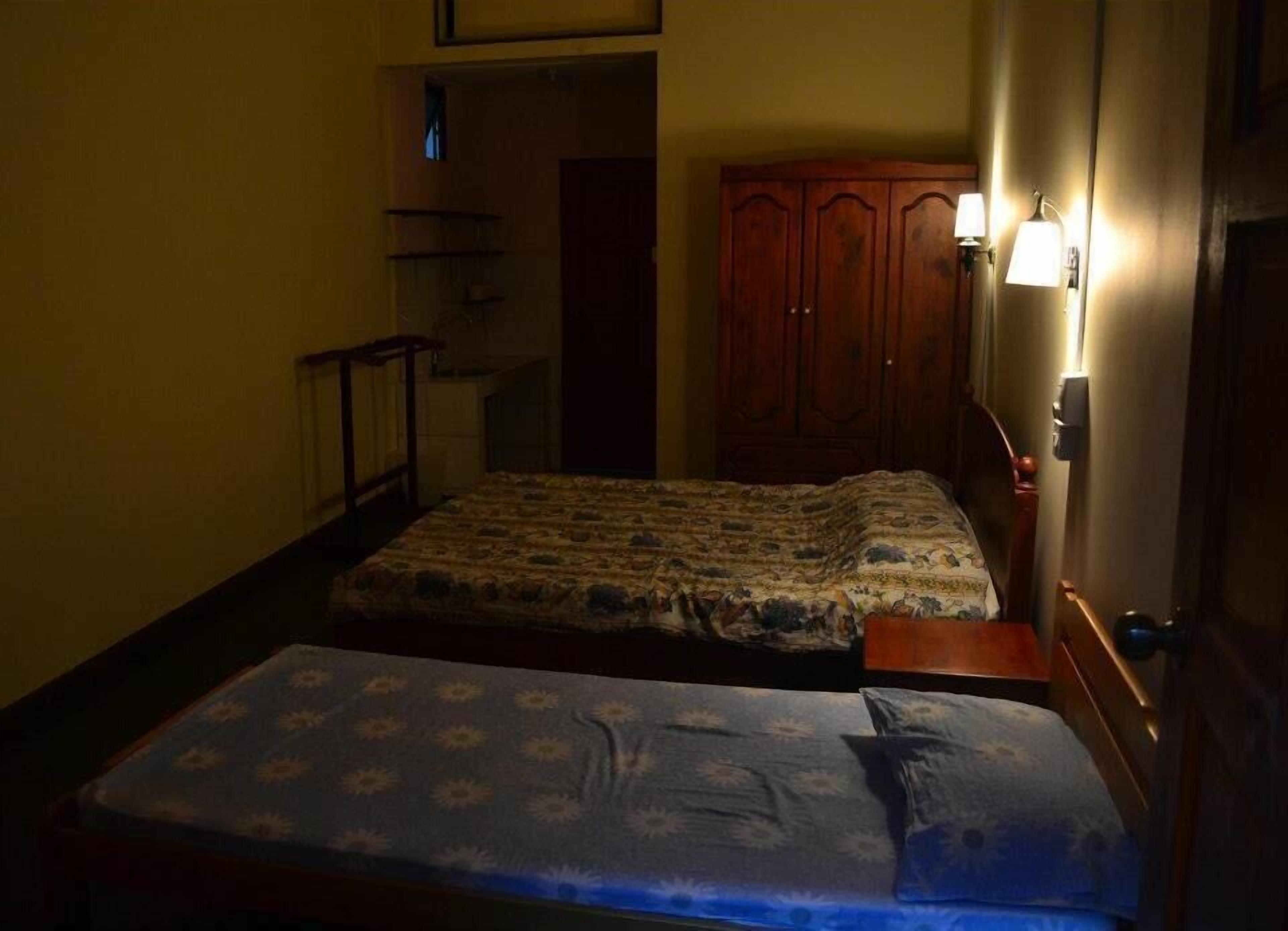 Una habitación pequeña y poco iluminada con una cama individual, un armario de madera y una pequeña mesa.