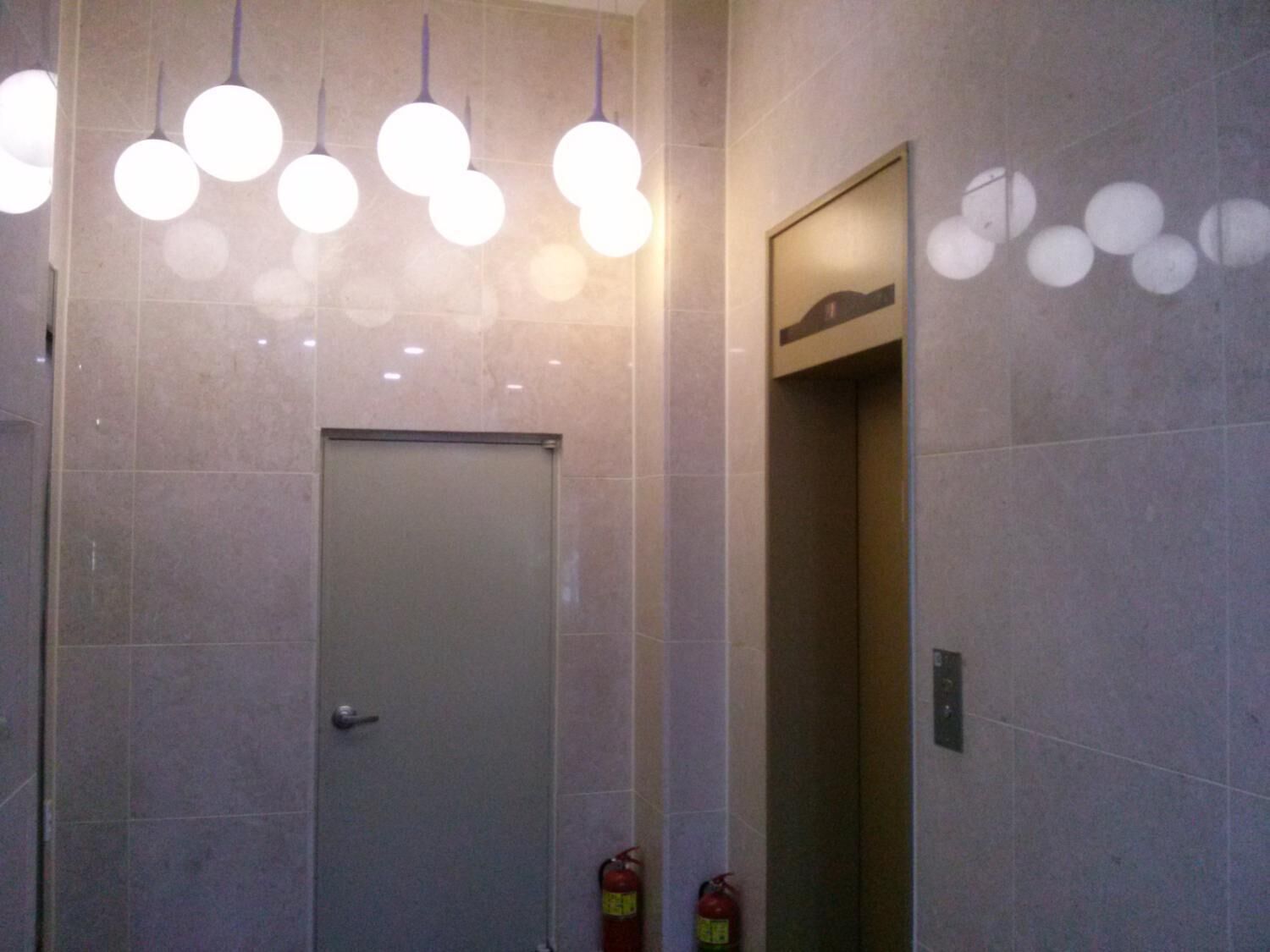 A modern bathroom with a door, tiled walls, and hanging spherical lights.