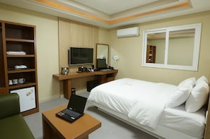 A hotel room with a bed, a desk with a laptop, a TV, a mirror, a wardrobe, and a minibar.