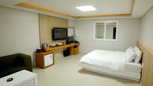 A hotel room with a bed, a desk with a computer, a television, and a small seating area. - Havana Hotel (Gwangju)