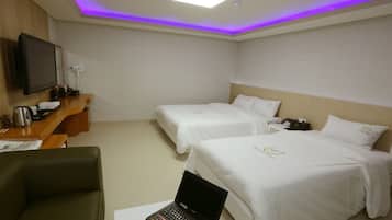 A hotel room with two beds, a desk with a laptop, a television, and a flat-screen TV mounted on the wall.