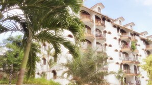 Un hotel de varios pisos con balcones, una palmera y un césped bien cuidado.