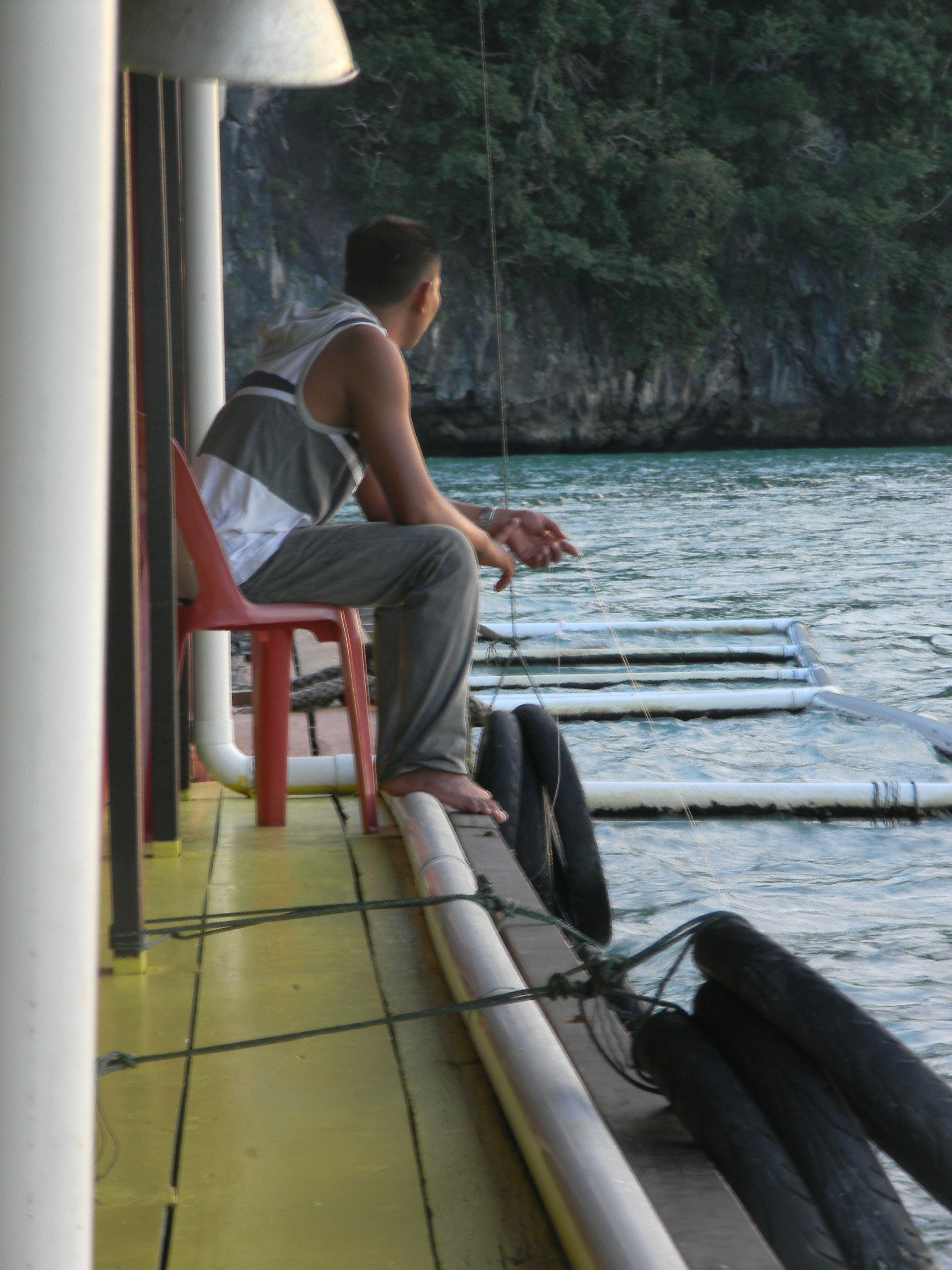 A person sitting on a red chair on a boat deck, holding a fishing line.