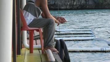 A person sitting on a red chair on a boat deck, holding a fishing line.