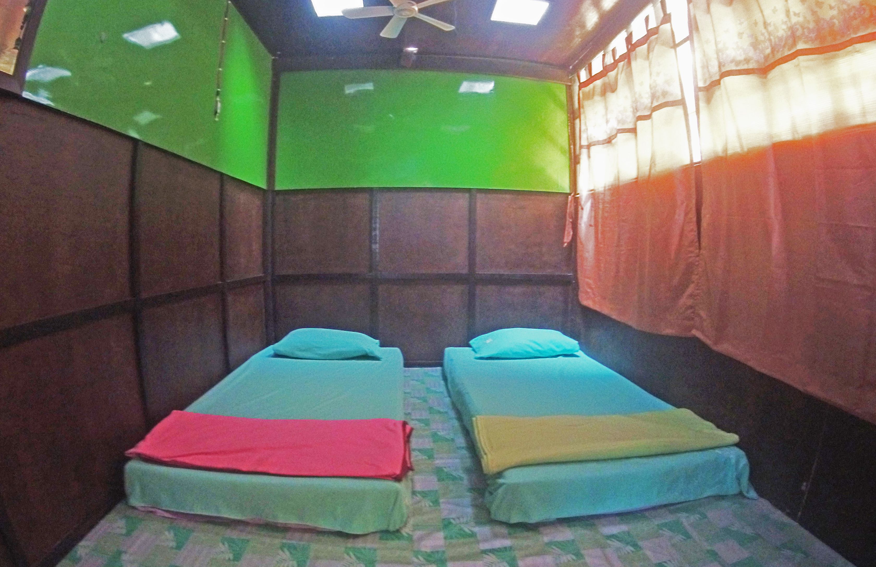 Ein Zimmer mit zwei Einzelbetten, einem Deckenventilator und einer grünen Wand.