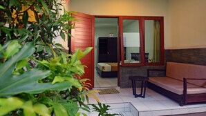 An outdoor seating area with a sofa and a table, a sliding glass door leading to a bedroom, and a potted plant in the foreground. - The Ayudya Glogor Carik (Denpasar)