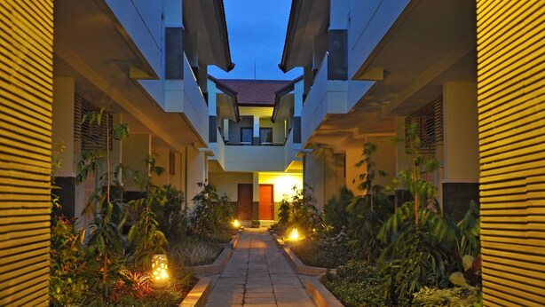 A corridor with a central walkway flanked by buildings, leading to a door at the end. - The Ayudya Glogor Carik (Denpasar)
