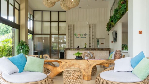Un hall de hotel con mostrador de recepción, mobiliario de mimbre y plantas de interior.