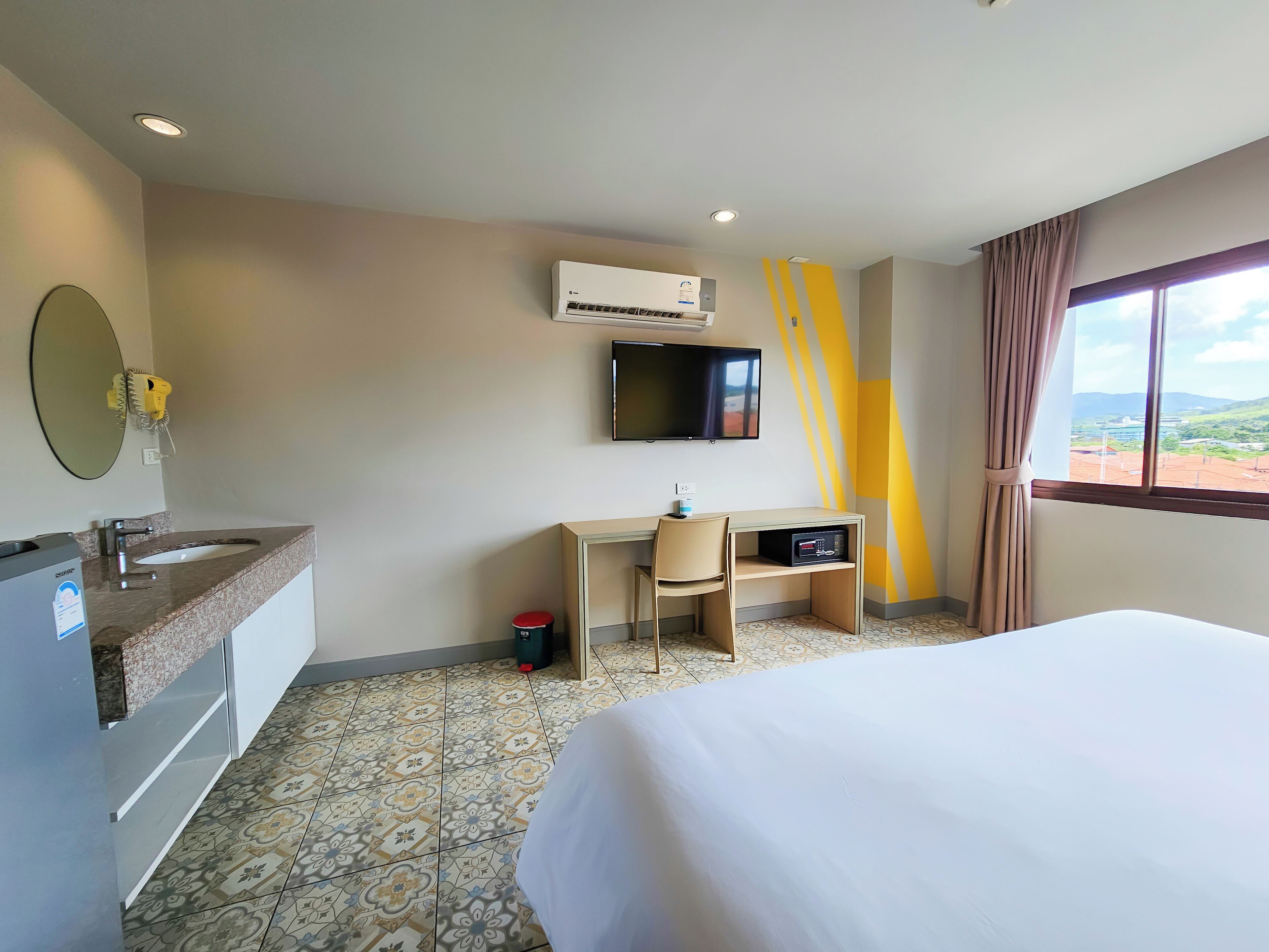 Habitación de hotel con cama, escritorio, silla, televisor, aire acondicionado y ventana con vista.