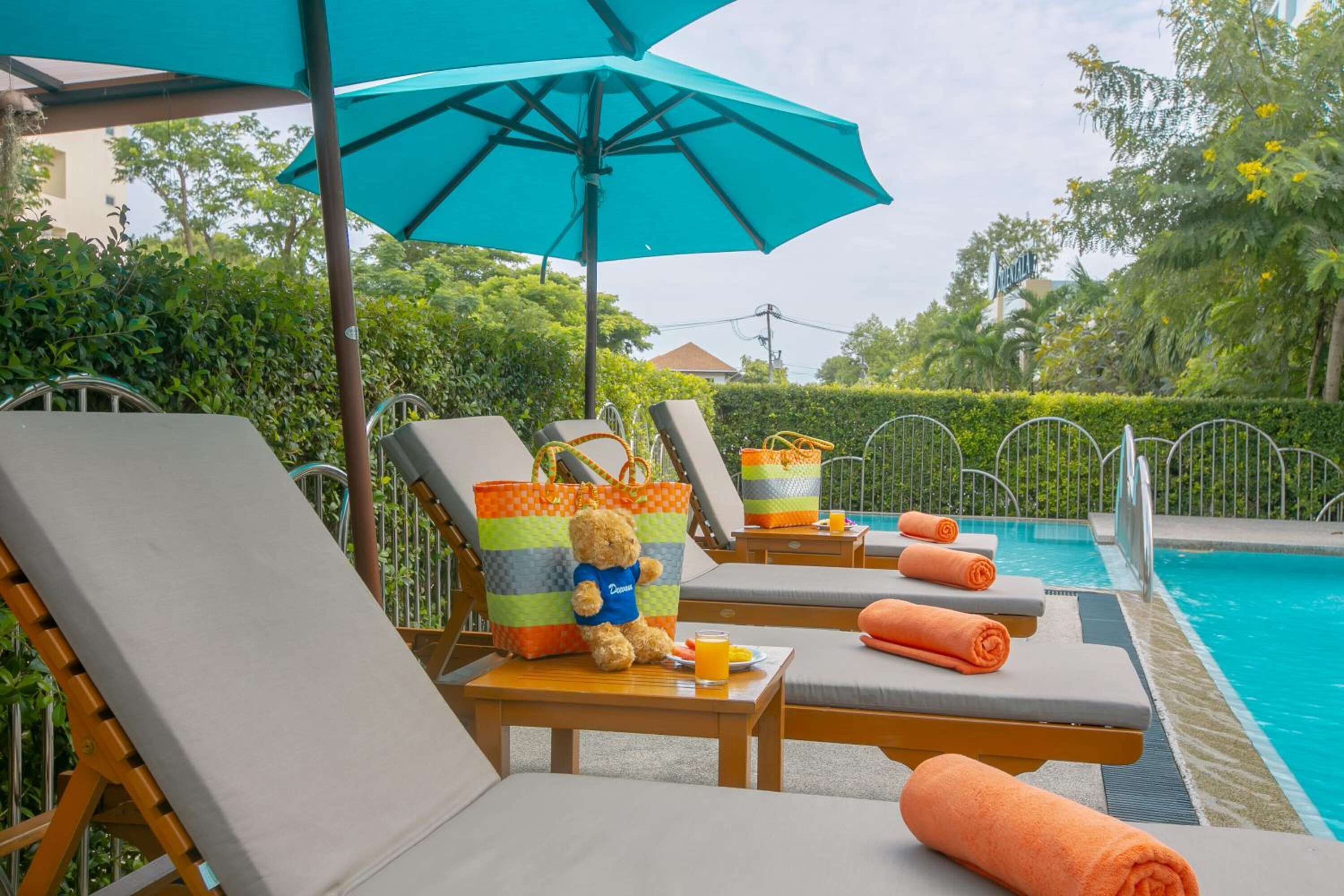 A poolside area with lounge chairs, a blue umbrella, and a teddy bear on a table.