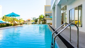 Una piscina con escalera metálica, rodeada por un edificio moderno con amplios ventanales y cielo despejado.