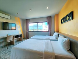 A hotel room with two beds, a desk, a flat-screen TV, and a window with curtains.