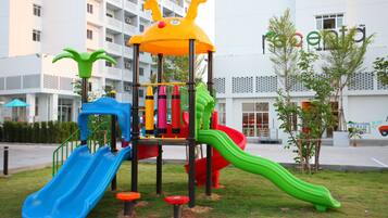 Un parque infantil con toboganes y estructuras para escalar, frente a un edificio con un letrero que dice 'recente'.