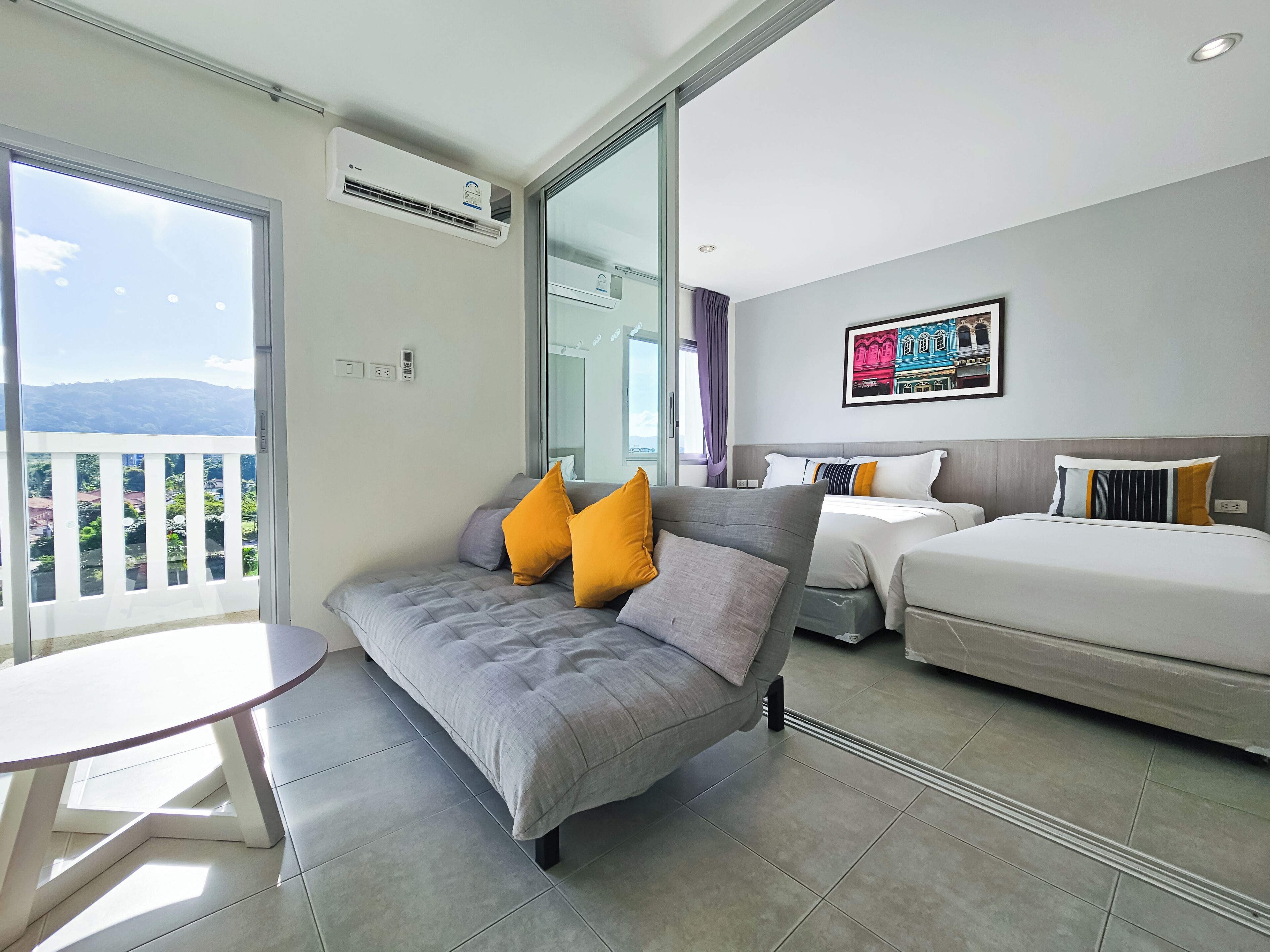 Una habitación de hotel moderna con balcón, un sofá con cojines, una cama con almohadas y un cuadro en la pared.