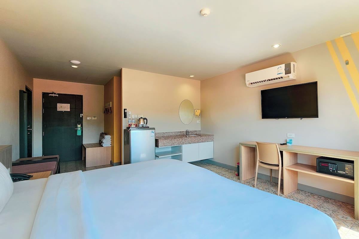A hotel room with a bed, a desk, a television, and an air conditioning unit.