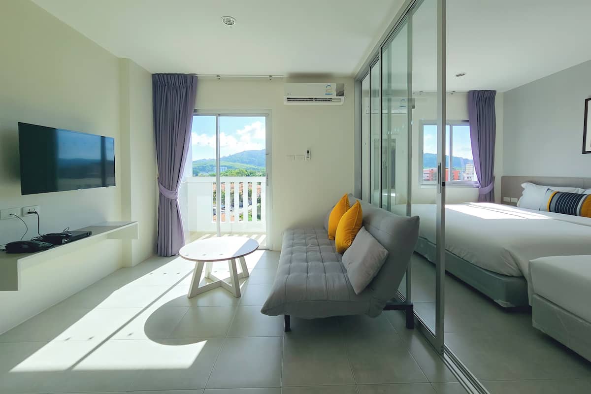A modern hotel room with a sofa, bed, TV, and a balcony with a city view.
