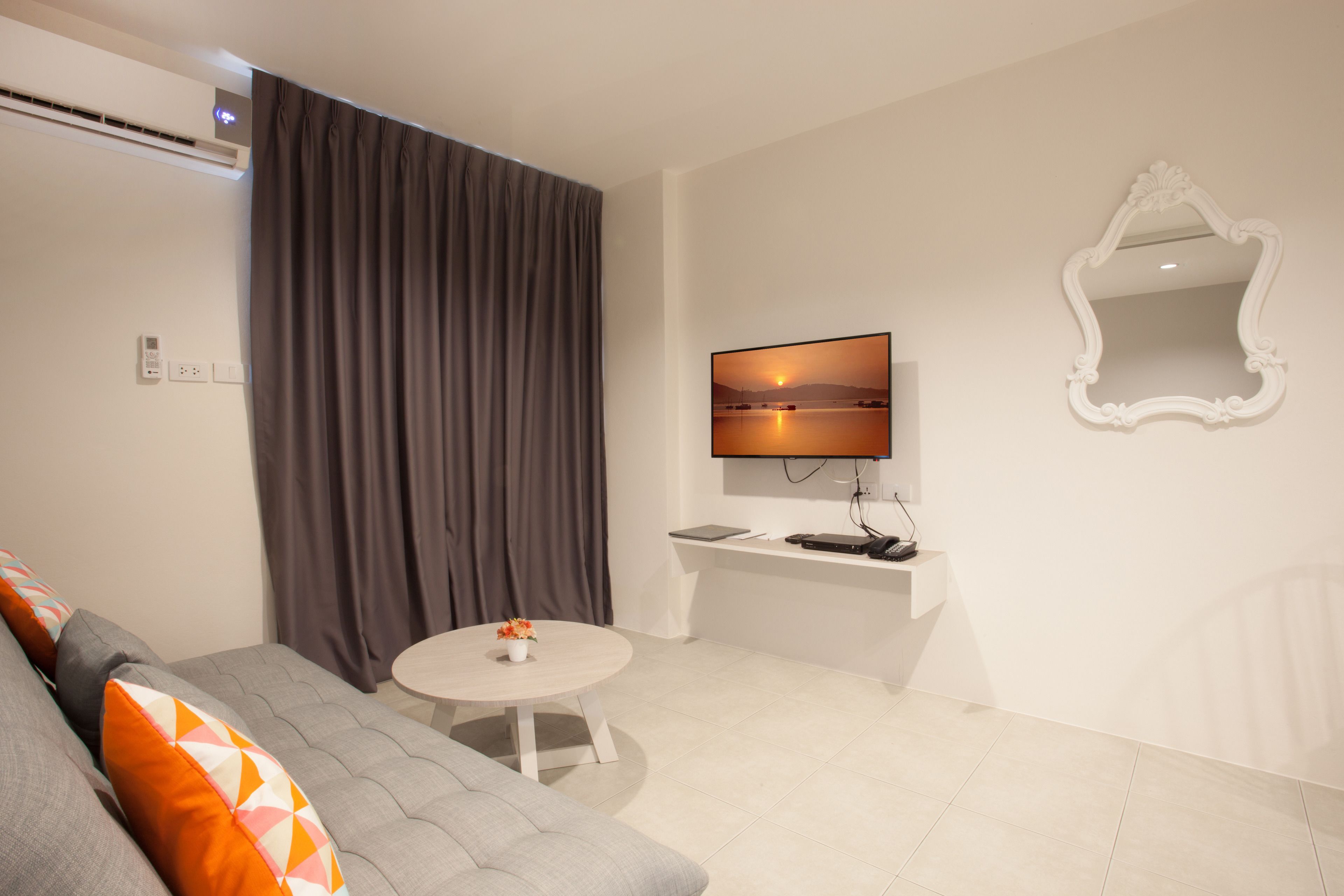A modern living room with a grey sofa, a round coffee table, a flat-screen TV mounted on the wall, and a white console table.