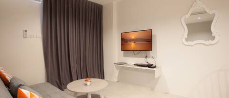 A modern living room with a grey sofa, a round coffee table, a flat-screen TV mounted on the wall, and a white console table.