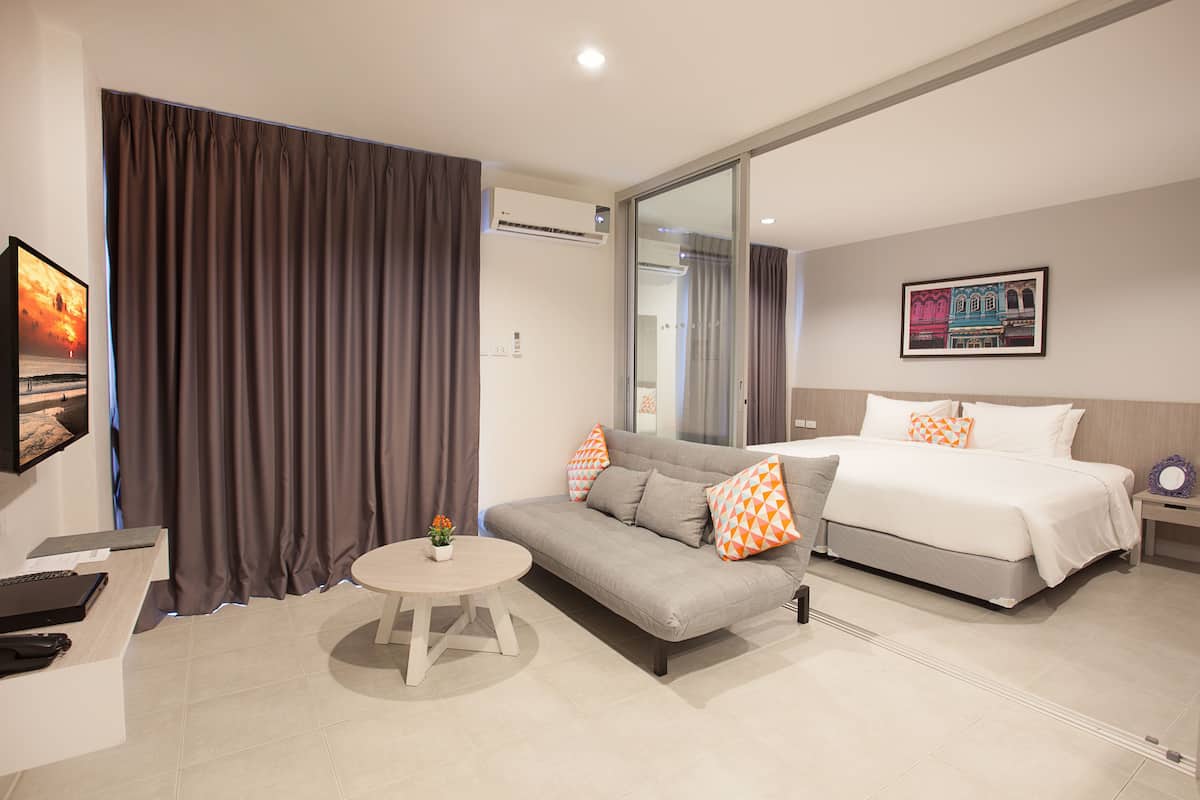 A modern hotel room with a sofa, a bed, a small table, and a large window.