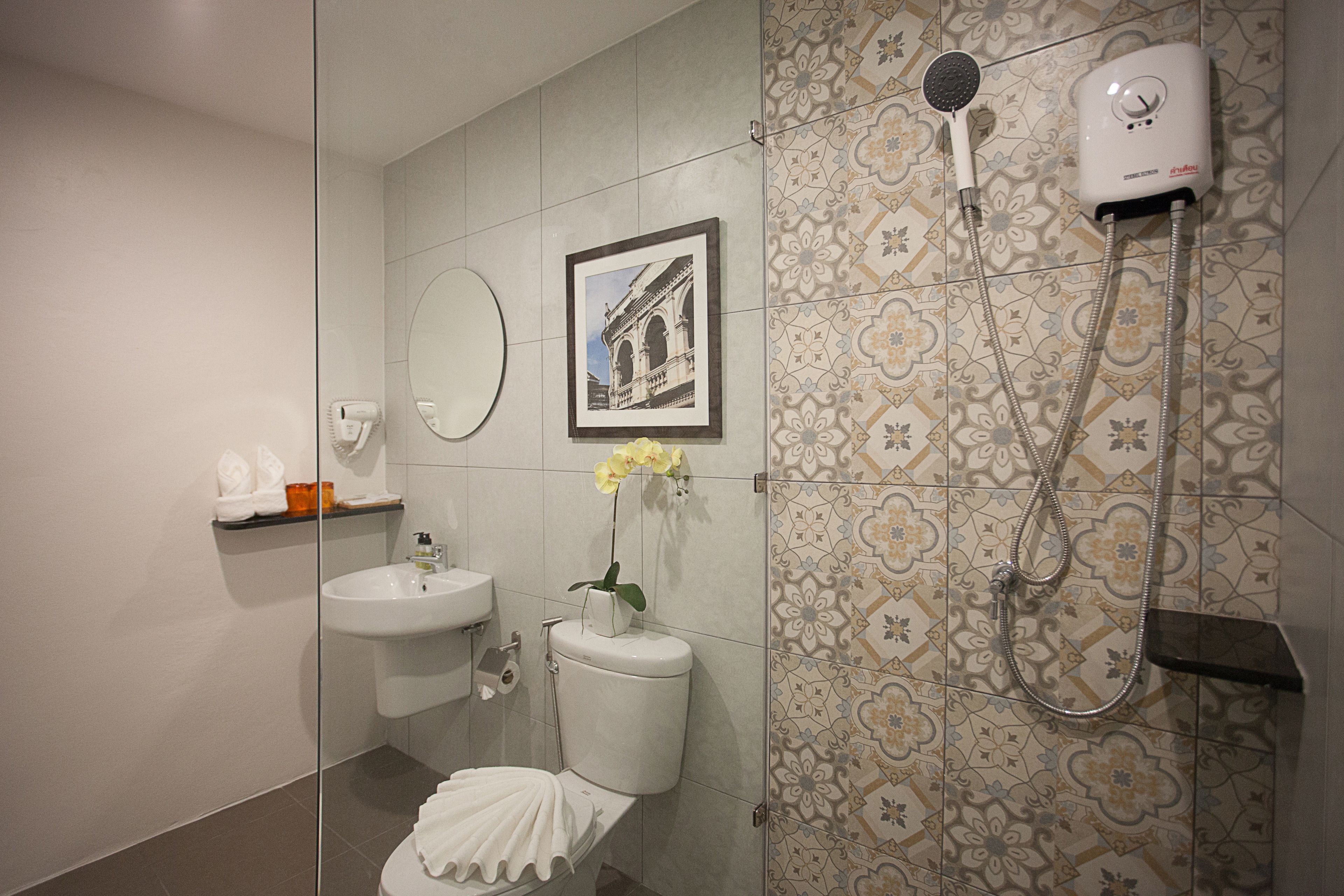 Ein Badezimmer mit Toilette, Waschbecken, Spiegel, Dusche und dekorativen Fliesen.