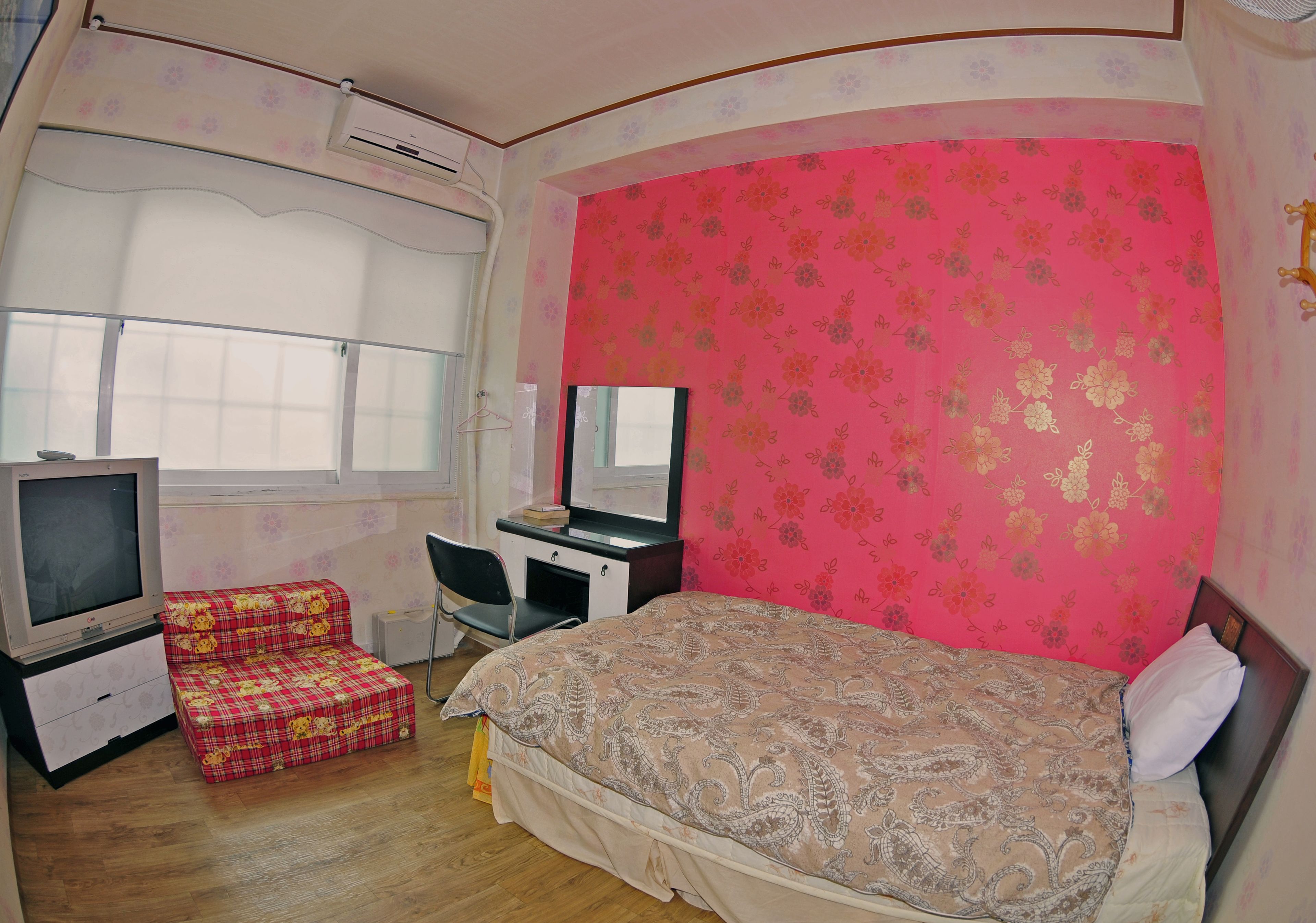 A bedroom with a bed, a desk, a chair, and a television.