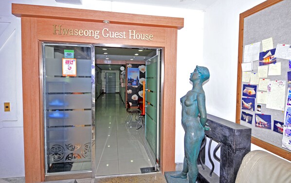 Der Eingang zum Hwaseong Guest House mit Glastür, Bronzestatue und einem Bulletinboard mit angepinnten Notizen.