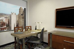 A hotel room with a city view, a desk with a lamp, a chair, and a TV on the wall. - Embassy Suites By Hilton Pittsburgh Downtown (Pittsburgh)