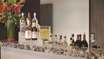 A bar area with bottles of liquor, a vase of flowers, and a glass container.