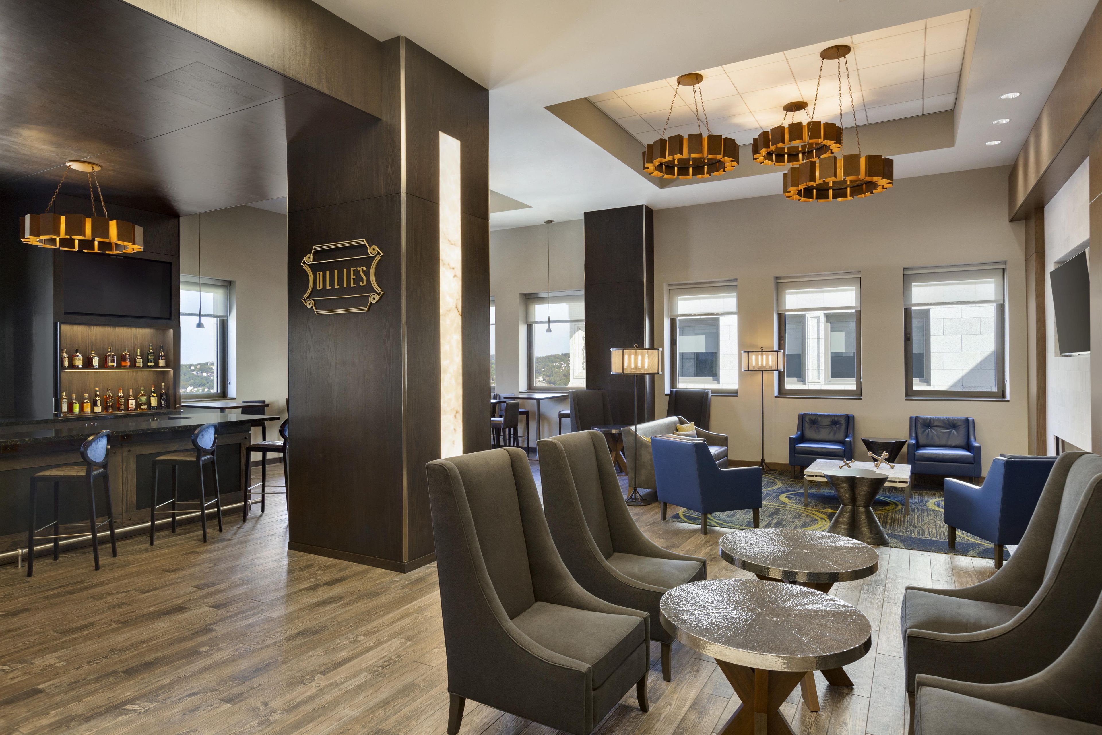 A modern bar area with a selection of liquor bottles, comfortable seating, and a large window providing natural light.