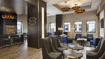 A modern bar area with a selection of liquor bottles, comfortable seating, and a large window providing natural light.