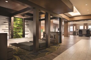 A spacious lobby with a high ceiling, a seating area with a sofa and chairs, and a large window with a view of greenery. - Embassy Suites By Hilton Pittsburgh Downtown (Pittsburgh)