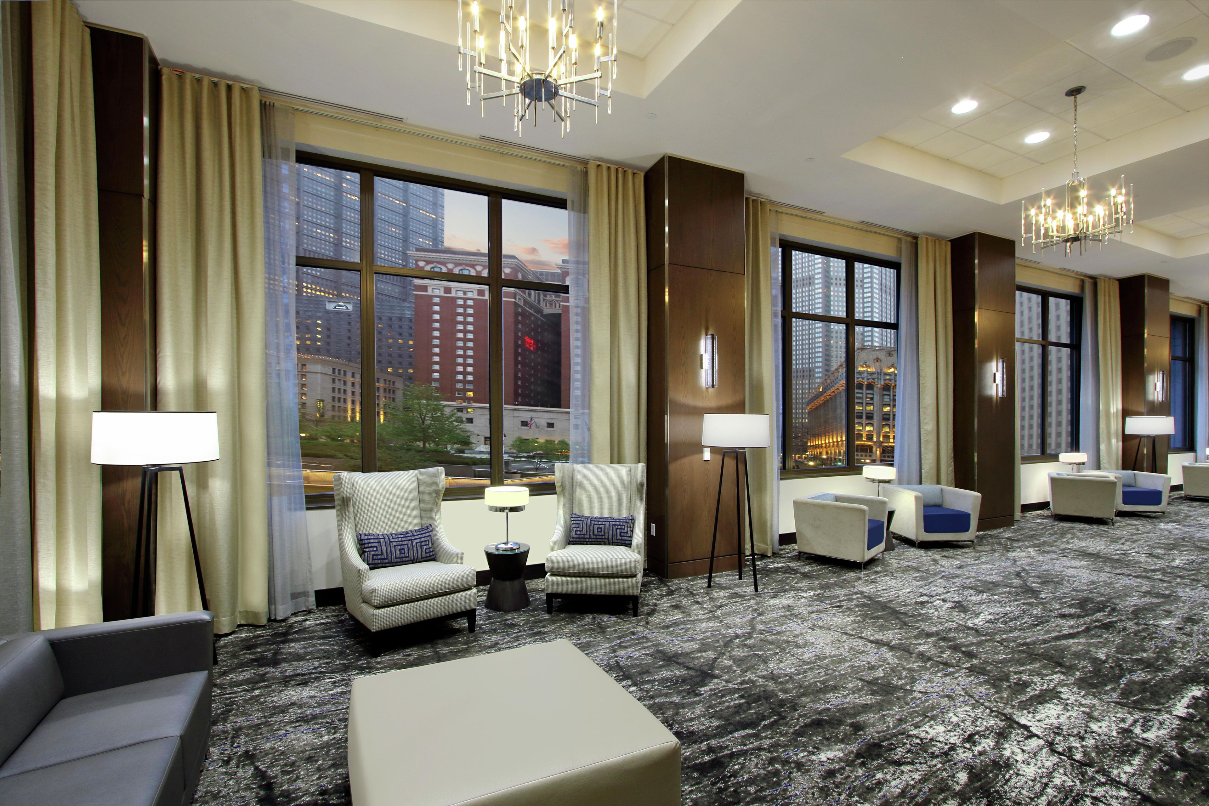 A hotel room with large windows, multiple seating areas, and a chandelier.